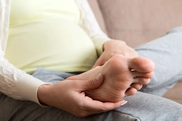 Leg cramps during pregnancy. Closeup of hands massaging swollen foot while sitting on sofa. — Stock Image Leg Cramps Pregnancy Closeup Hands Massaging Swollen Foot While Sitting Stock Picture