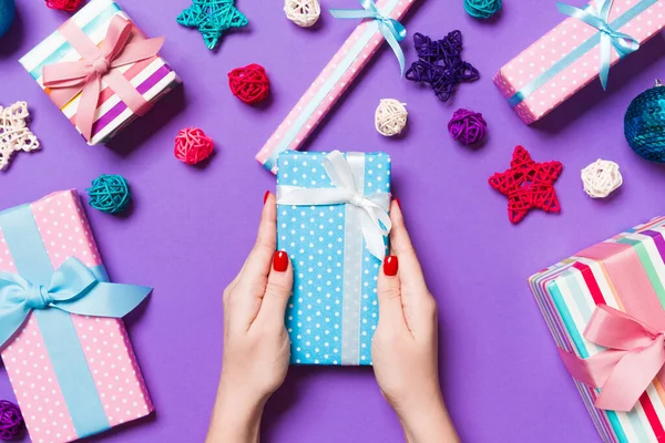 お祝いの紫色の背景にクリスマスプレゼントを保持する女性の手のトップビュー 休日の装飾 おもちゃやボール 年末年始のコンセプト — ストック写真