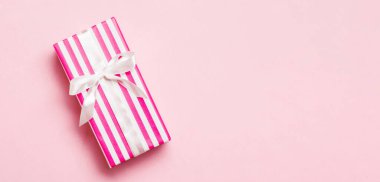 Pembe arka planda beyaz kurdeleli el yapımı Noel hediyeleri. Şimdiki kutu, renkli tabloda hediye süslemesi, kopya alanı ile üst görünüm.