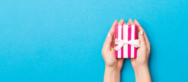 Woman arms holding gift box with colored ribbon on blue table background, top view and copy space for you design.