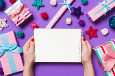 Kadın elinin rengarenk arka planda notlar aldığına dair üst görünüm. Yeni yıl süslemeleri ve oyuncakları. Noel zamanı konsepti.