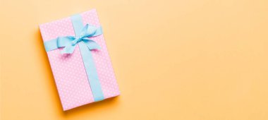 Noel 'i ya da diğer tatil hediyelerini turuncu arka planda mavi kurdeleli kağıda sardım. Şimdiki kutu, renkli tabloda hediye süslemesi, kopya alanı ile üst görünüm.