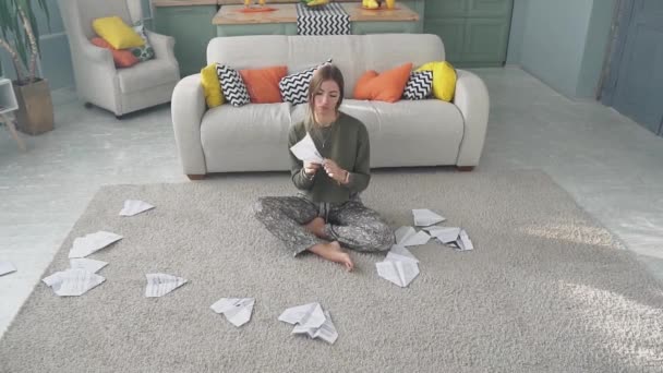 Szomorú lány elindít egy papírrepülőt a földön ülve. — Stock videók
