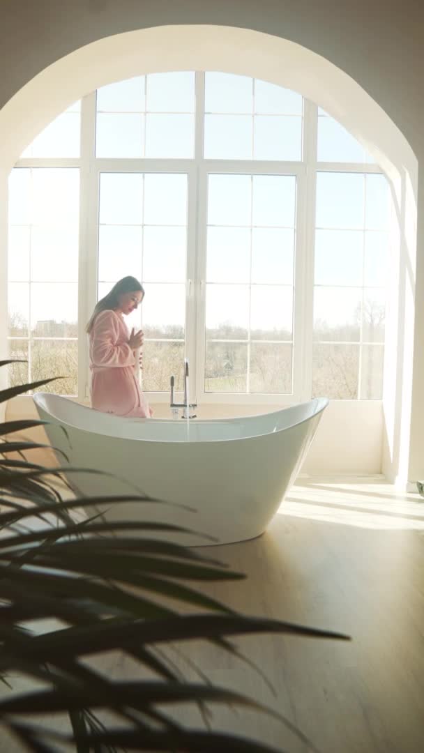 Egy gyönyörű fiatal nő készít egy pihentető fürdőt egy napos reggelen. — Stock videók