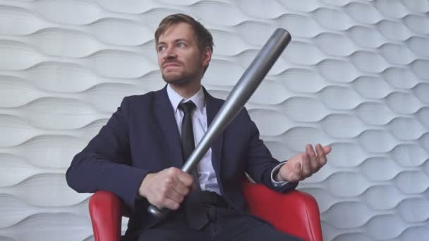 Boze man met een honkbalknuppel zittend op een rode stoel — Stockvideo