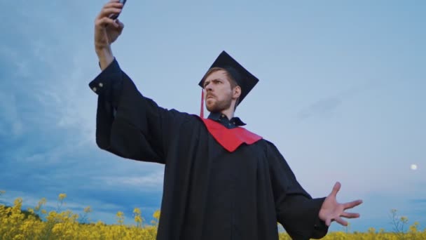 Podekscytowany absolwent robi zabawne selfie na smartfonie w parku — Wideo stockowe