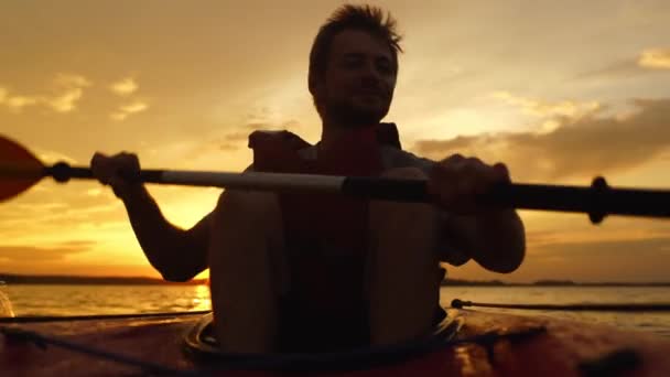 Ein aktiver, athletischer junger Mann segelt auf einem Boot gegen den Sonnenuntergang. — Stockvideo