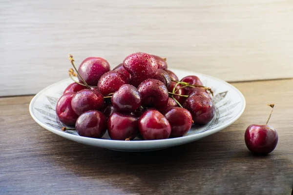 Ahşap bir masa üzerinde bir plaka üzerinde taze lezzetli kiraz meyve