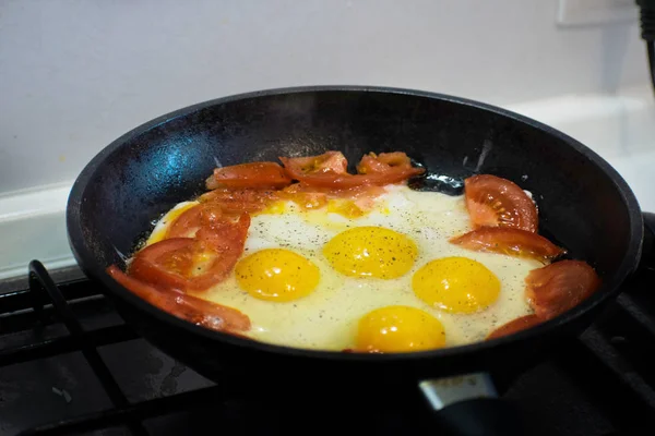 Fried eggs with tomato in a frying pan. Fried eggs with tomatoes. Top view.