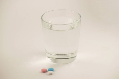 Bir bardak su ve beyaz zemin üzerine hap. Bir bardak su ve vitamin.