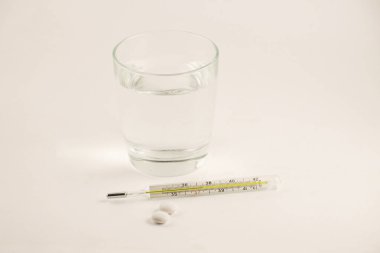 Bir bardak su, hap ve beyaz arka plan üzerinde termometre. Cam Merkür termometre ile yüksek bir sıcaklık.