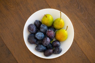 Olgun armut ve Erik beyaz bir plaka üzerinde yalan.