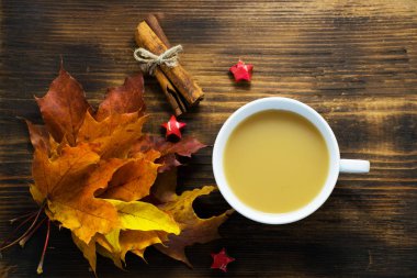Bir fincan sıcak kahve süt ve baharat ve sonbahar tahta masada bırakır. Cappuccino kahve ile akçaağaç yaprakları.