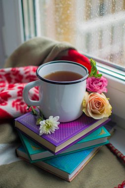 Rahat natürmort: bir fincan sıcak çay, kitap ve pencere üzerinde sıcak ekose çiçeklerle.