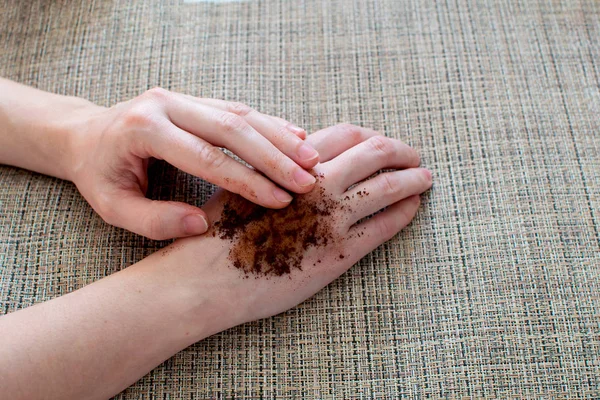 Woman hand with scrub coffee grounds on table.