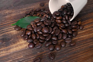 Ahşap tahta üzerinde yaprak ve fincan ile kahverengi Arabica kahve çekirdekleri.