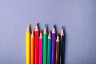 Gri arka planda çok renkli bir kalem. Renkli kalemler bir sırada yatıyor. Okul için kalemler.