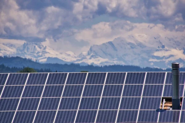 Evin çatısındaki güneş panelleri ve ufuktaki karla kaplı dağlar.