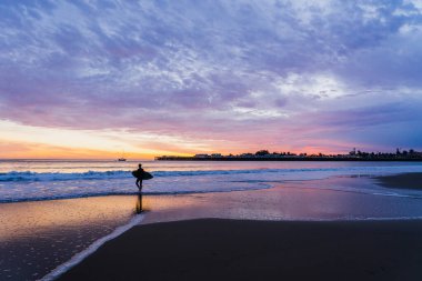 Santa Cruz, Kaliforniya 'da güzel bir günbatımında elinde sörf tahtası olan bir sörfçünün silueti.