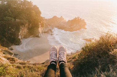 McWay Falls, Big Sur 'da sonbahar günbatımında. Julia Pfeiffer Burns Eyalet Parkı. Şelaleye dayanmış bir turistin ayakları