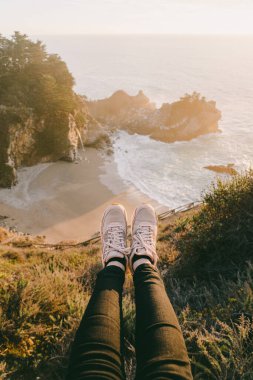 McWay Falls, Big Sur 'da sonbahar günbatımında. Julia Pfeiffer Burns Eyalet Parkı. Şelaleye dayanmış bir turistin ayakları