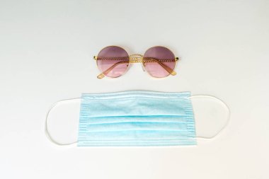 Beyaz arka planda güneş gözlüğü ve mavi yüz maskesi. Yaz tatili aksesuarlarıyla düz kompozisyon. Coronavirüs nedeniyle 2020 'de seyahat eğilimleri ve kurallar