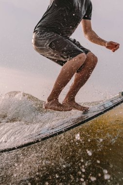 Sportif bir adam bir teknenin arkasındaki sörf tahtasında sörf yapıyor. Yaz tatili için nehirde uyanış vakti. Sörf tahtasına zıplayan ayakların yakın çekimi