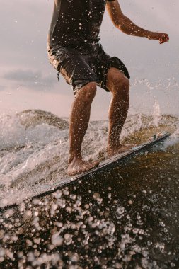 Sportif bir adam bir teknenin arkasındaki sörf tahtasında sörf yapıyor. Yaz tatili için nehirde uyanış vakti. Ayaklar sörf tahtasına yakın çekim