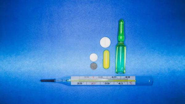 Termômetro médico e pílulas de cor em um fundo azul. Indicações 36.6 — Fotografia de Stock