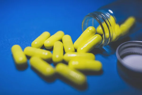 파란색 배경 및 투명 유리 약국 병에 노란색 약. 선택적 초점 — 스톡 사진