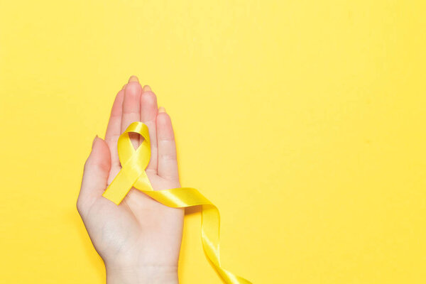 Female hand holding yellow ribbon on color background. Cancer concept