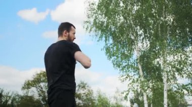 Güçlü sporcu, güzel bir gökyüzü olan yeşil ağaçların arka planında antrenman yapmadan önce ellerini ısıtır..