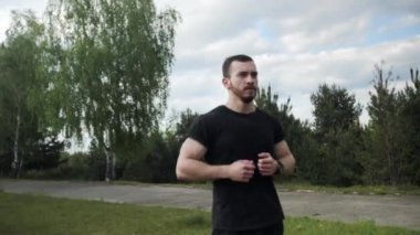 Güçlü, kaslı, sağlıklı bir adam hemen ısınıyor ve güzel bir gökyüzü olan yeşil ağaçların arka planına atlıyor..