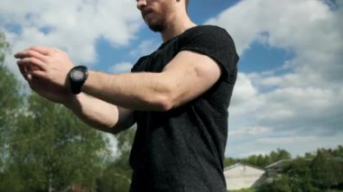 Kaslı atletik bir adam, güzel bir gökyüzü olan yeşil ağaçların arka planında antrenman yapmadan önce ısınma hareketleri yapar..