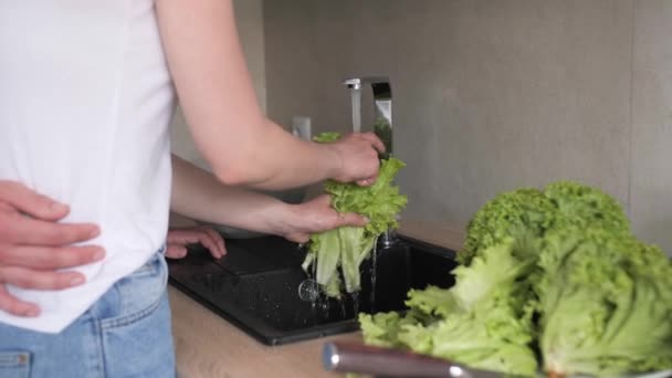 Close up Pareja joven lava verduras verdes frescas en una cocina moderna . — Vídeo de stock