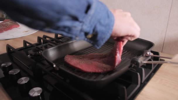 Mannen lägger stor kalvstek på en varm grillpanna i köket. — Stockvideo