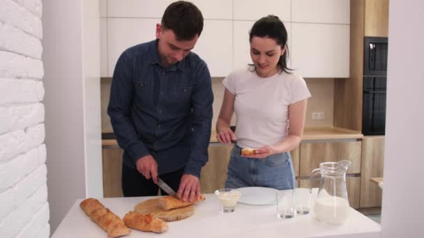 Beau couple dans la cuisine frotte baguette avec du beurre sur une cuisine blanche . — Video