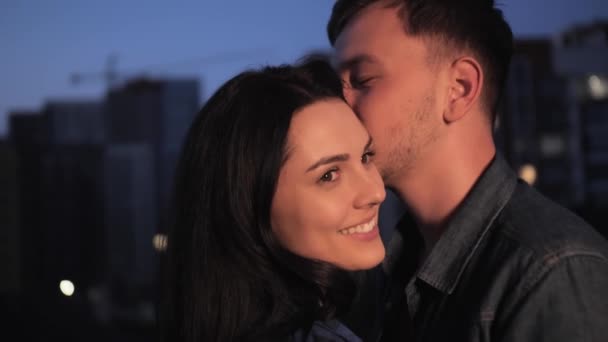 Ευτυχισμένο νεαρό ζευγάρι αγκαλιάζει χαμογελώντας και φιλιά στο φόντο της πόλης βράδυ. — Αρχείο Βίντεο