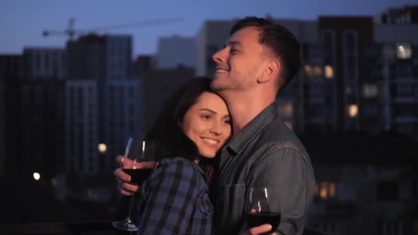 Glada unga par kramas leende och dricka vin på kvällen stad bakgrund. — Stockvideo
