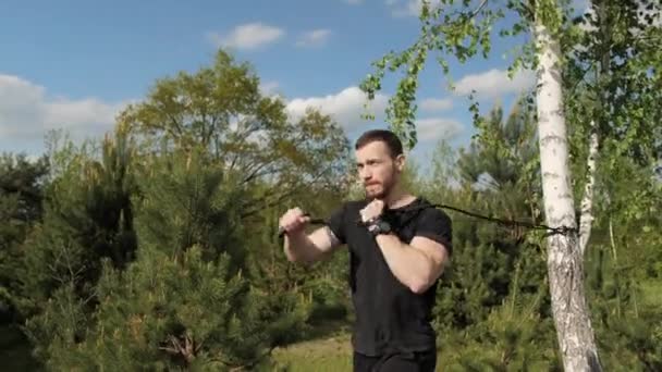 Conceito de treino de força. Homem forte fazendo exercícios usando borracha, musculação treino com borracha ao ar livre . — Vídeo de Stock