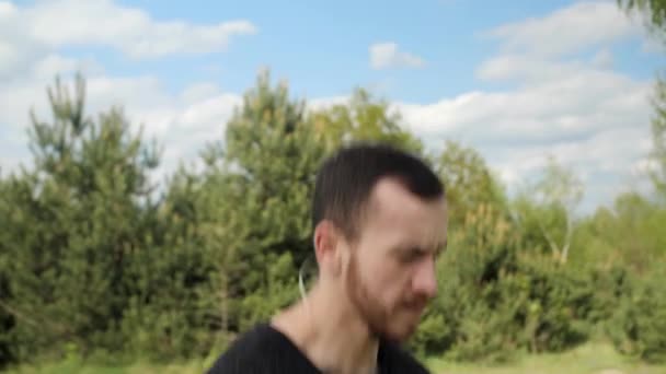 Mann mit Muskulatur macht Aufwärmläufe auf der Stelle und springt auf einem Hintergrund grüner Bäume mit schönem Himmel. — Stockvideo