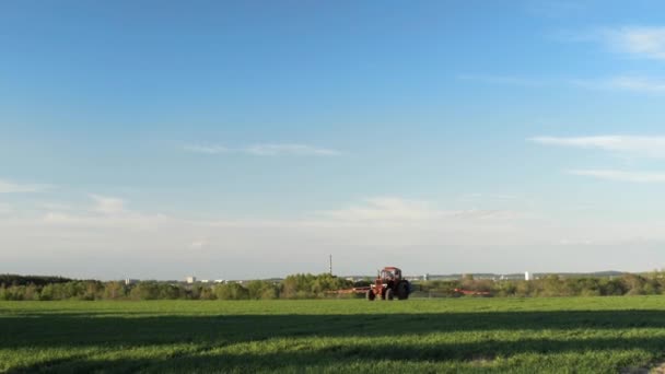 Tracteur travaillant dans un champ avec herbe verte, ciel bleu, journée ensoleillée . — Video