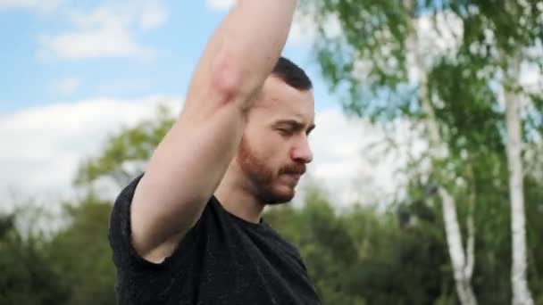Man met gespierde doet warming-up zwaai je handen op een achtergrond van groene bomen met een prachtige lucht. — Stockvideo