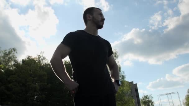 Close up Silný svalnatý kulturista s vousy procházky kolem stadionu proti podsvícení a modré obloze. — Stock video