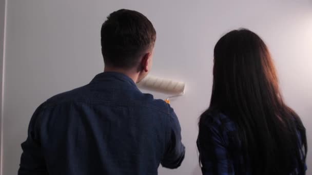 Fiatal pár festi a fal fehér egy új apartmanban.Szobafelújítás otthon. — Stock videók