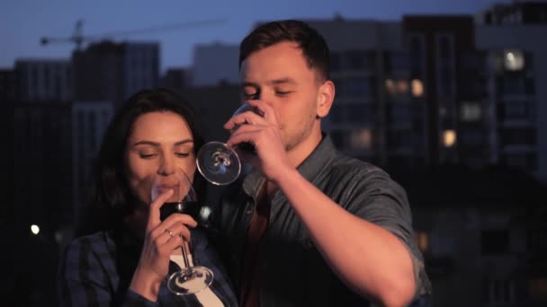 Joyeux jeune couple embrassant souriant et buvant du vin sur fond de ville du soir . — Video