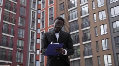 Gözlüklü Afro-Amerikalı bir mühendis, arka plandaki güzel evlerde mavi bir tablet tutuyor..