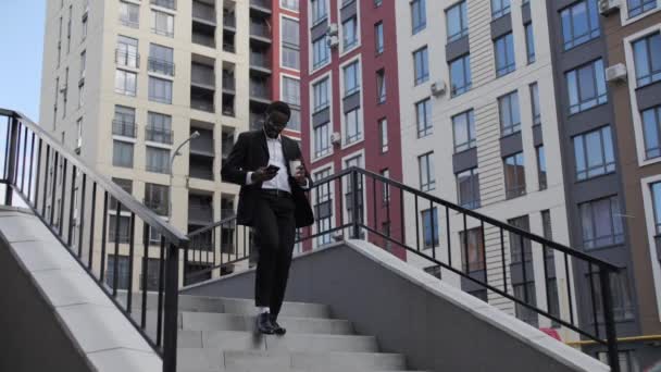 African American man goes down stairs with coffee and while reads message. — Stock Video