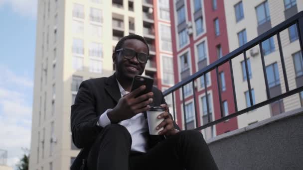 Close up view of Handsome afro american sitting on stairs with coffee and talking on video link. — Stock Video