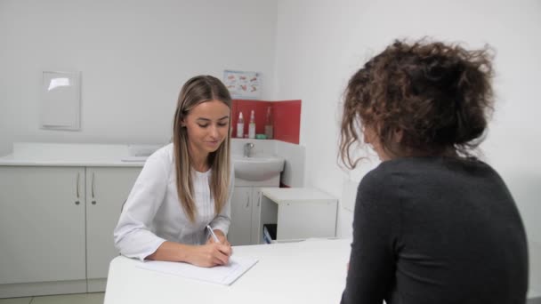 Ginecólogo atractivo femenino asesora al cliente en esta área en una clínica de cosmetología . — Vídeos de Stock